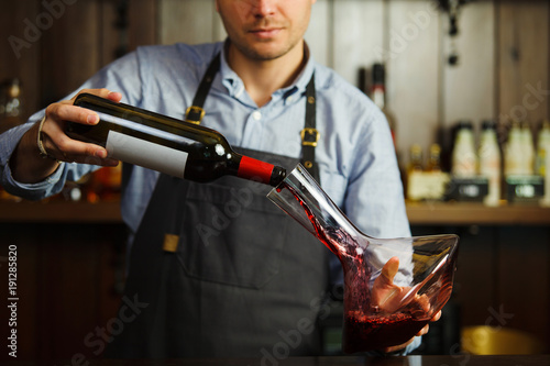Sommelier pouring wine into glass from decanter. Male waiter