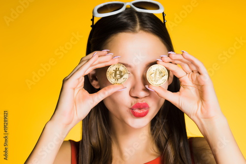 funny young girl holding golden bitcoins by the eyes