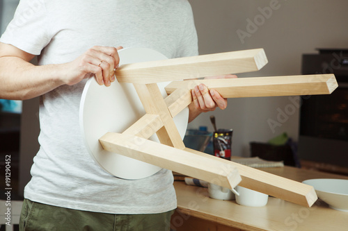 Man holding in hands wooden stool  carefully examining seat