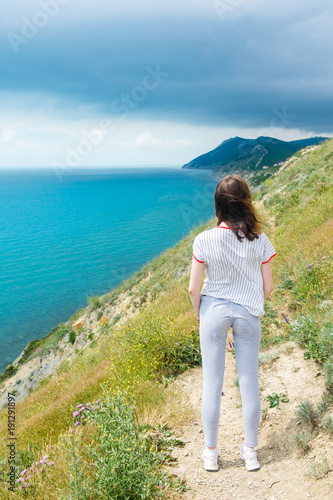Young woman worth of grief and looks at sea, back view.