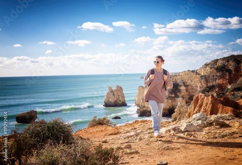 A traveler with a backpack walks along the rocky coast of the ocean, admiring the incredible scenery. Portugal, the Algarve, a popular destination for travel in Europe