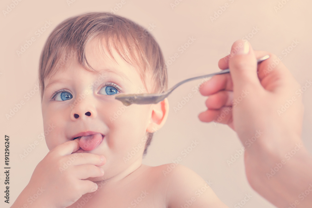 Small blue-eyed blond baby boy during feeding from a spoon Small blue-eyed blond baby boy during feeding from a spoon