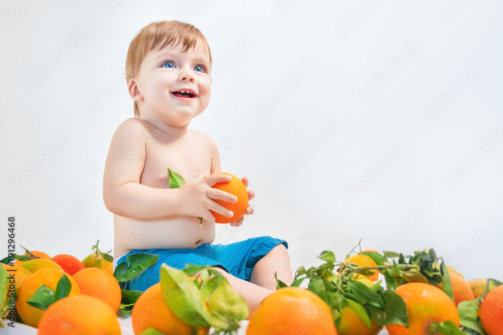 Smiling blue-eyed blond baby boy sitting surrounded by oranges Smiling blue-eyed blond baby boy sitting surrounded by oranges