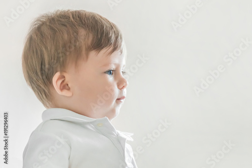 Portrait of a blonde baby boy with blue eyes in a white polo shirt on a gray background