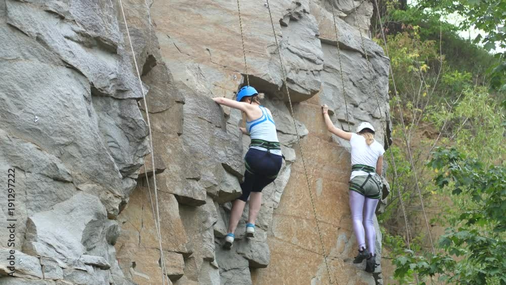 Two women climbers climb up the rock. Close-up shot, two girls, rock, green trees. Two women climbers climb up the rock. Close-up shot, two girls, rock, green trees.