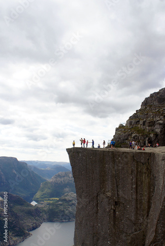 People on the edge of Preikestolen cliff (Prekestolen or Pulpit Rock) at fjord Lysefjord, beautiful landscape of norwegian nature, sunny day, popular travel landmark in Forsand, Norway 