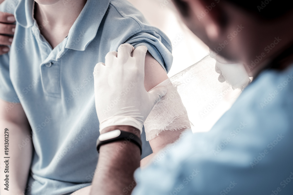 Fototapeta premium Taking care of you. Scaled up look on a male doctor putting a bandage on an arm of a patient after checking him and making diagnosis.