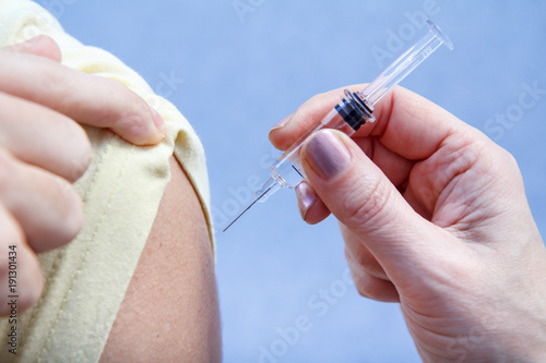 Hand of doctor holding syringe for vaccination to upper arm of patient