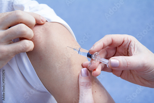 Doctor holding syringe for vaccination to upper arm of patient
