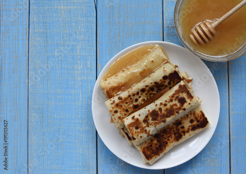  space for text. Pancakes with honey on a blue retro wooden background. Pancakes and honey Maslenitsa. A pile of pancakes, honey, for the celebration of the carnival. Thin pancakes for breakfast.
