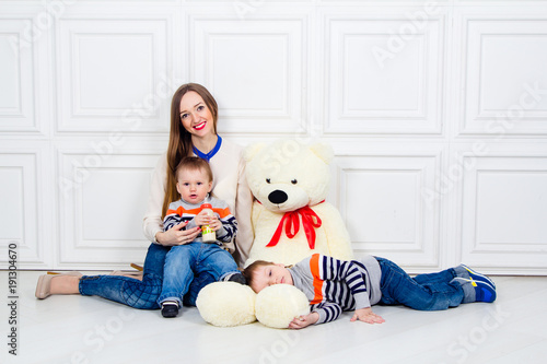 Fototapeta Naklejka Na Ścianę i Meble -  young mother with two children and Teddy bear. family happiness, mom and two sons in jeans sitting on the floor
