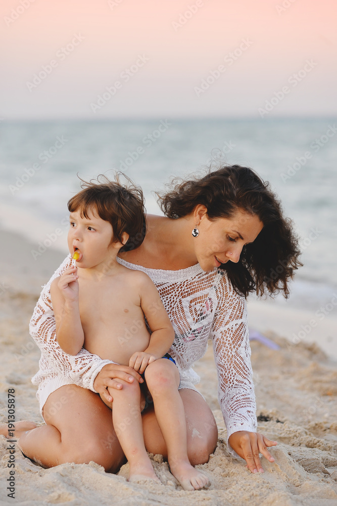Fototapeta premium mom with baby sitting on the beach and playing sand in summer