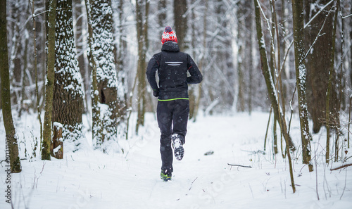Image from back of running athlete among trees in winter forest