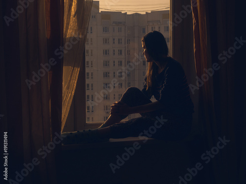 Profile Shot Of Sad Woman Sitting On Window Sill at Sunset Time on the Background of a Panel Building