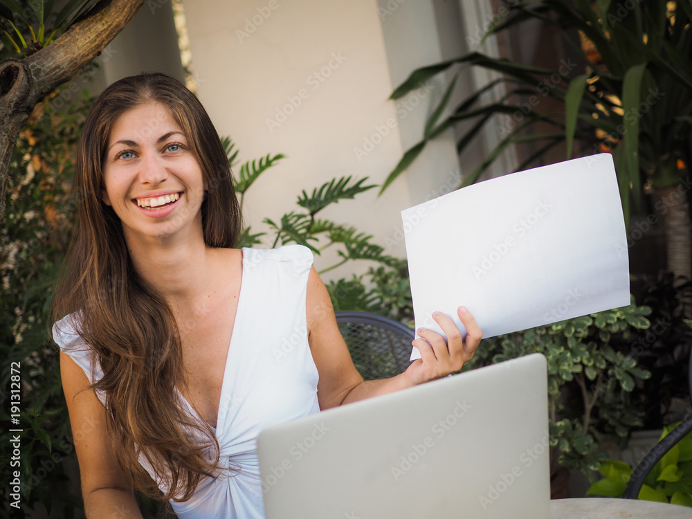 smiling woman working with laptop at an outdoor garden holding white paper smiling woman working with laptop at an outdoor garden holding white paper