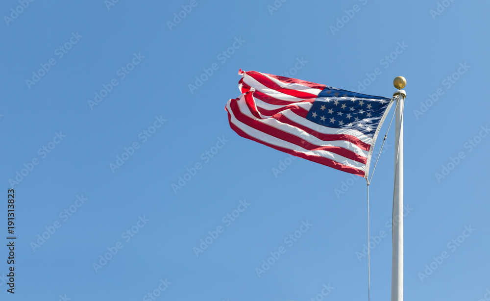 The United States flag on blue sky bacground, turned to the left
