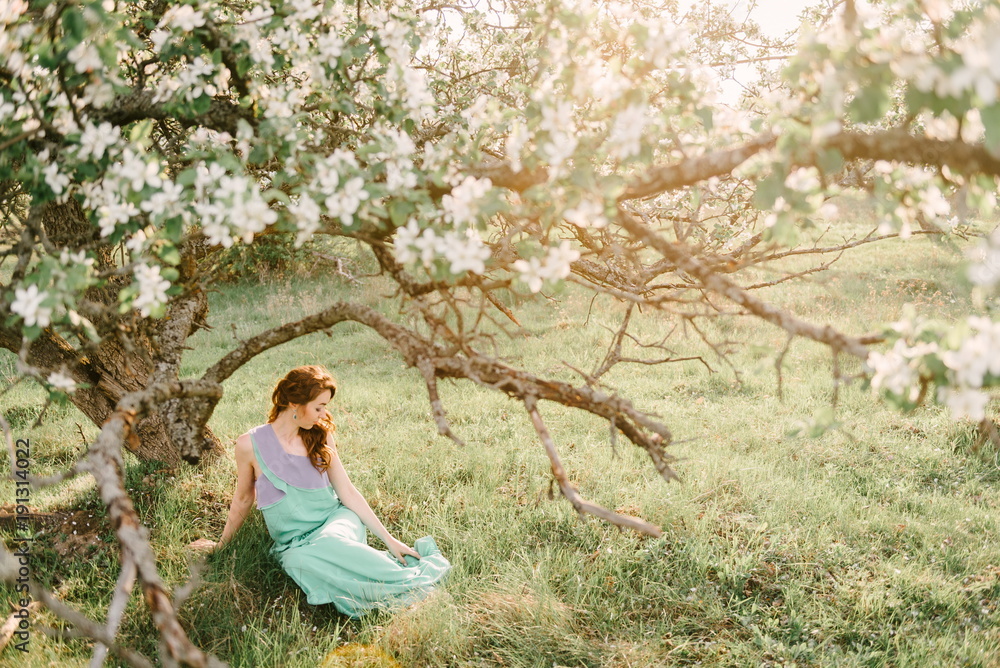 A girl in spring in a flowering apple orchard sits under the crown of an apple tree A girl in spring in a flowering apple orchard sits under the crown of an apple tree