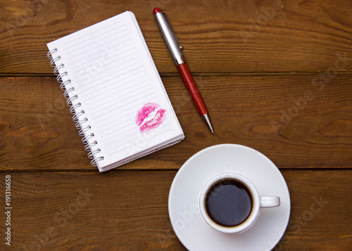 open blank notebook with a trace of lipstick on a wooden table with a cup of coffee
