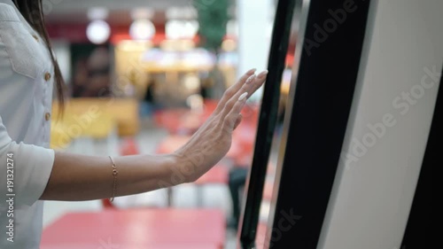 Caucasian female using automated teller machine with big digital screen while standing in shopping mall, woman verifies account balance on banking application via modern device icon photo
