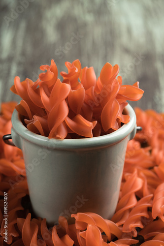 Lentil spiral. Closeup of a bowl full of uncooked red lentil fusilli on a rustic wooden table. Vertical. Copy space. Healthy concept food. Diet. Orange pasta. photo