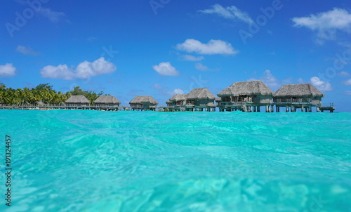 Over water bungalows with thatched roof in a tropical lagoon, seen from sea surface, Tikehau atoll, Tuamotus, French Polynesia, Pacific ocean, Oceania