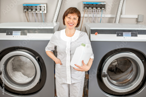 Portrait of a senior washwoman in uniform standing near the washing machines in the hotel laundry