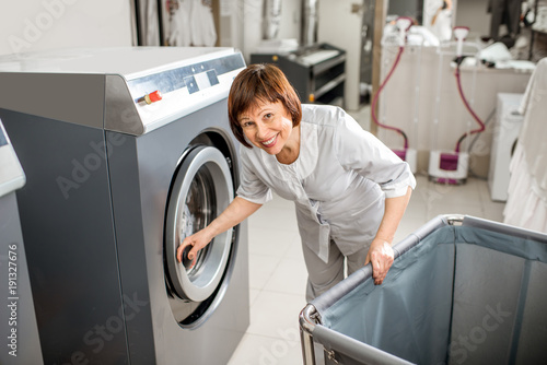 Photography Portrait of a senior washwoman opening professional washing machine in the laund