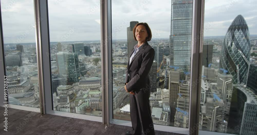 4K Portrait smiling mature businesswoman in London city office. View from the window shows famous skyline with iconic buildings. Slow motion. 4K Portrait smiling mature businesswoman in London city office. View from the window shows famous skyline with iconic buildings. Slow motion.