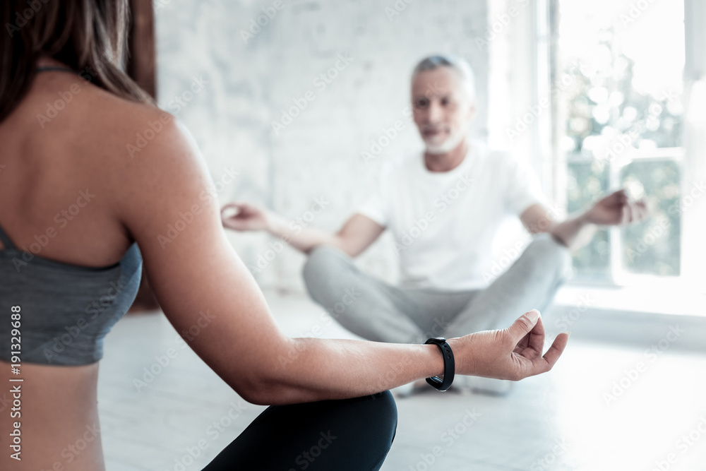 Obraz premium Active retirement. Selective focus on a young lady teaching mature man yoga while both sitting on their mats and meditating in a yoga class.