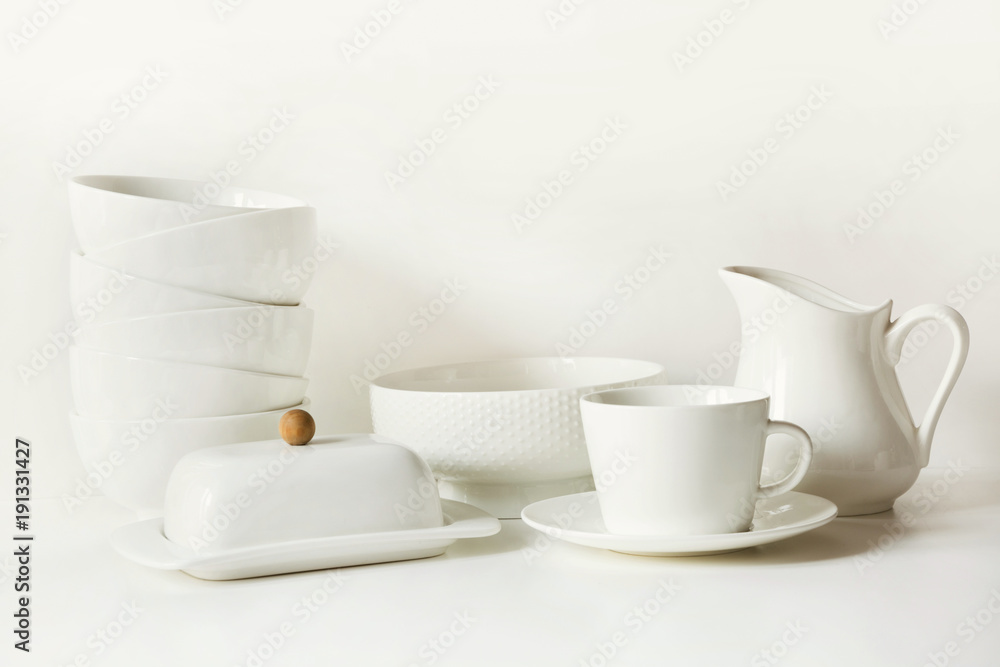White tableware for serving. Crockery,dish, utensils and other different white stuff on white table-top. Kitchen still life as background. Copy space. White tableware for serving. Crockery,dish, utensils and other different white stuff on white table-top. Kitchen still life as background. Copy space.