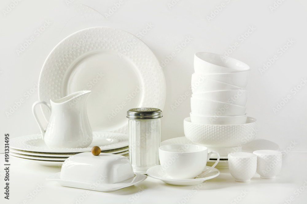 White tableware for serving. Crockery,dish, utensils and other different white stuff on white table-top. Kitchen still life as background. Copy space. White tableware for serving. Crockery,dish, utensils and other different white stuff on white table-top. Kitchen still life as background. Copy space.