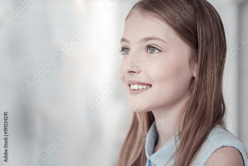 On cloud nine. Beautiful long-haired grey-eyed girl smiling and emitting happiness with her smile while looking in the distance and thinking about something