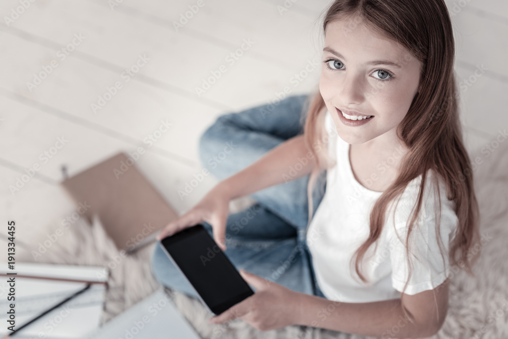 My phone. Beautiful smiling long-haired girl wearing jeans and a white shirt and holding her black phone while sitting on the floor and her stuff in the background My phone. Beautiful smiling long-haired girl wearing jeans and a white shirt and holding her black phone while sitting on the floor and her stuff in the background