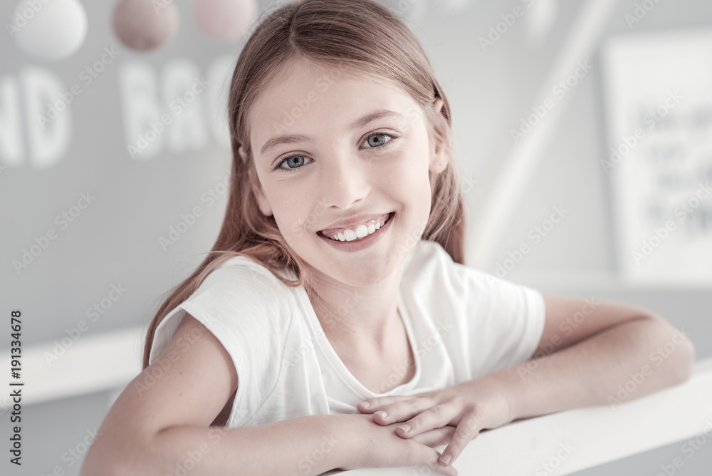 In high spirits. Good-looking long-haired grey-eyed girl smiling and emitting happiness with her smile while wearing a white t-shirt In high spirits. Good-looking long-haired grey-eyed girl smiling and emitting happiness with her smile while wearing a white t-shirt