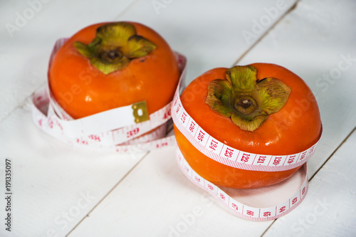 In selective of  the persimmon at the right side with measuring tape around persimmon,beside blurred other persimmon,on wooden timber board blurry light aorund. photo