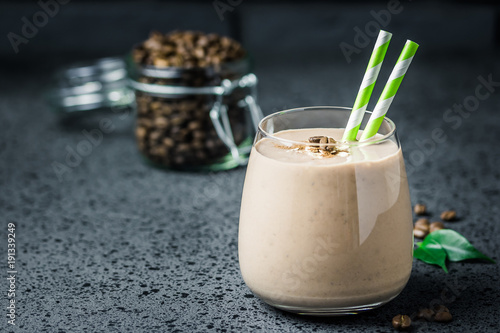 Chocolate mocha breakfast smoothie and coffee beans in glass jar on dark concrete background. Selective focus, space for text. 