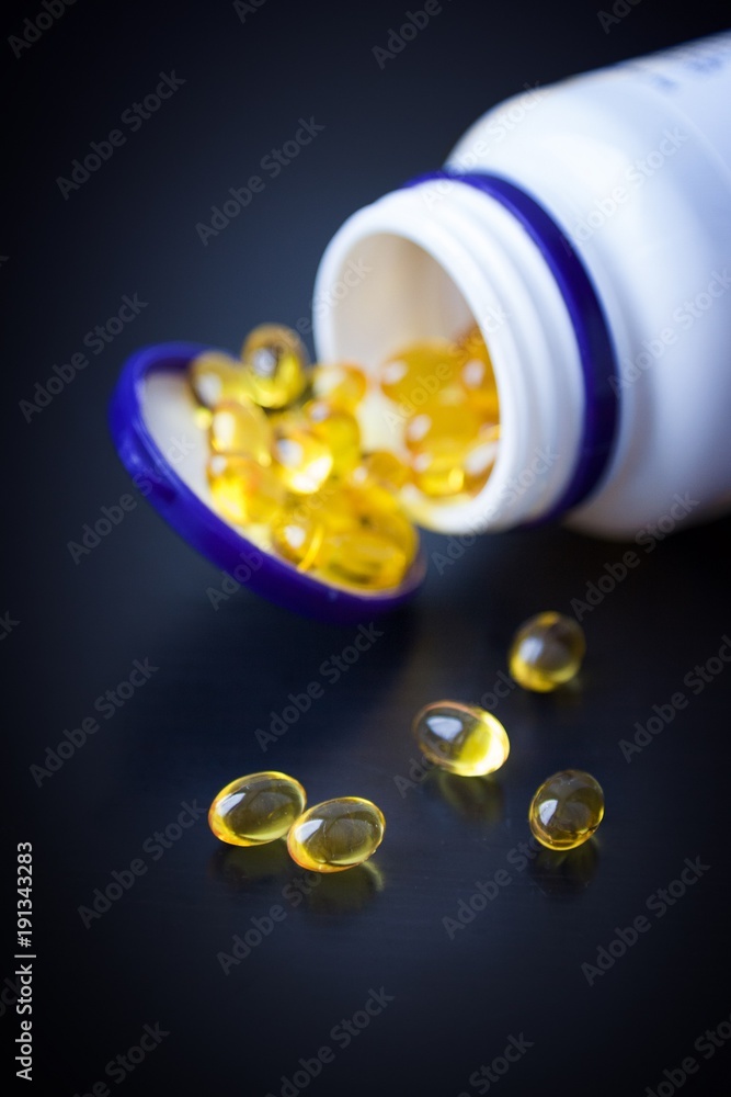 Capsules of fish oil in gold cup on black background Capsules of fish oil in gold cup on black background