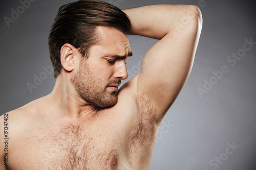 Close up portrait of a shirtless man smelling his armpit