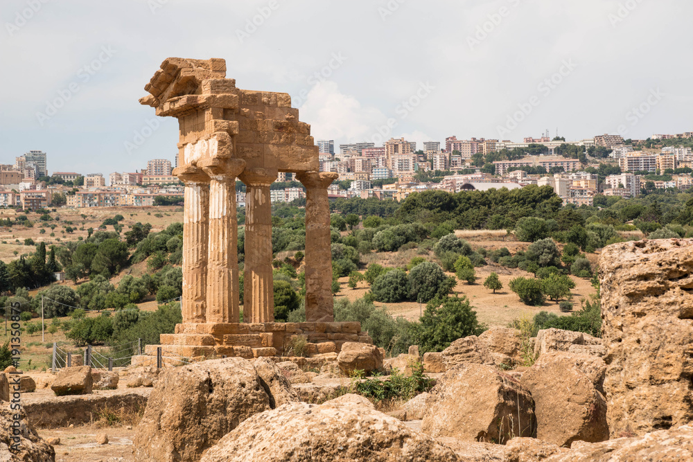 The re-assembled remains of the Temple of Castor and Pollux with Agrigento city in the background. Valle dei Templi - temples Valley, Agrigento, Italy.