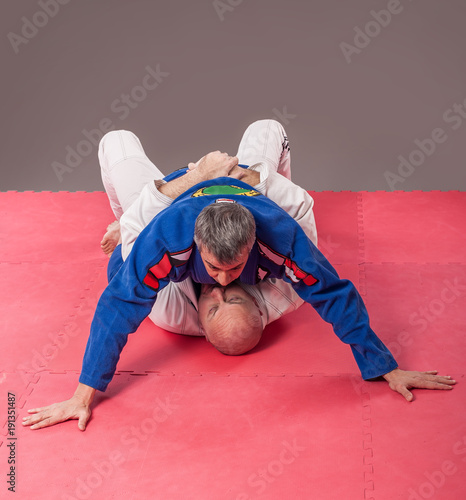 Brazilian jiu-jitsu instructor in traditional kimono show ground mount position photo