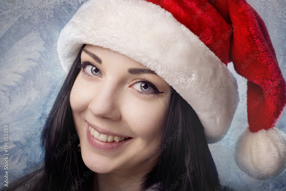Brunette girl in Santa hat smiling on a background of blue winter patterns Brunette girl in Santa hat smiling on a background of blue winter patterns