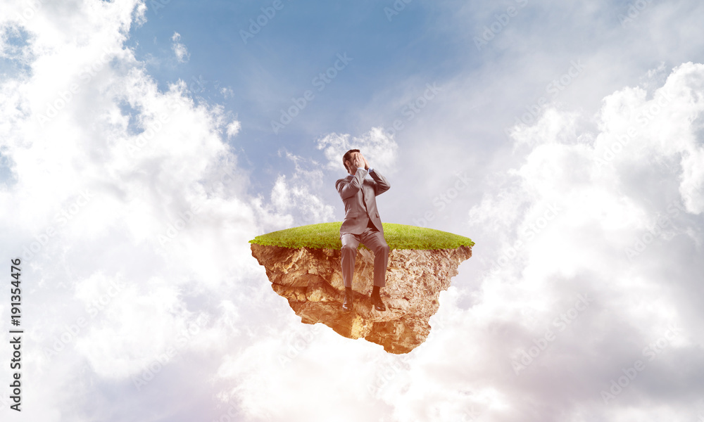 Young man on floating island in blue sky do not want to see anything Young man on floating island in blue sky do not want to see anything