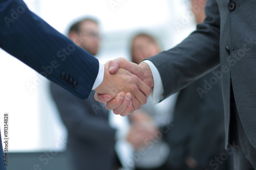 Two businessmen shaking hands with colleagues on background.