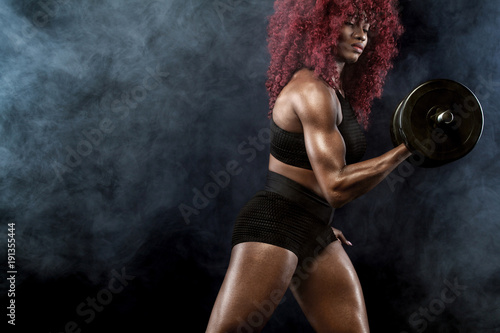 Sporty beautiful woman with dumbbells makes fitness exercising at black background to stay fit