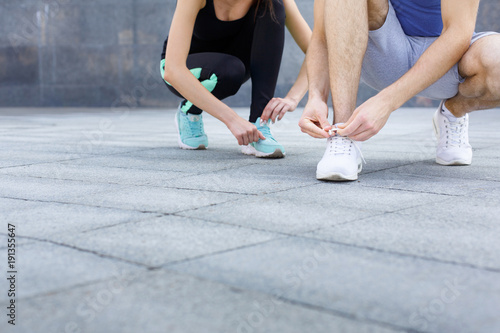 Unrecognizable man and woman tying shoelaces before running