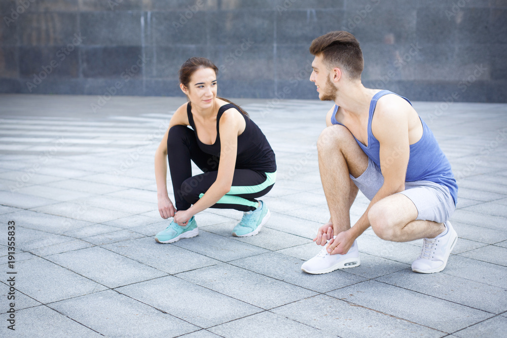 Happy man and woman tying shoelaces before running
