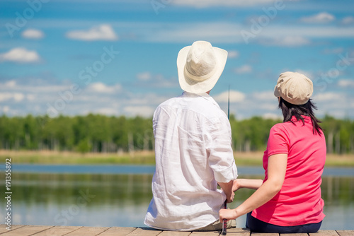 family couple with a fishing rod sitting on a wooden pier near the lake, rear view © kosmos111