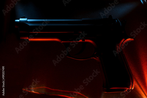 Pistol. Against the background of blue and red shades of material. Light effect.