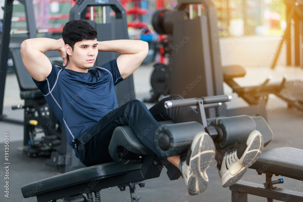 Fototapeta premium Asian sport man doing sit-ups on the floor in gym. man exercising in fitness gym for good health. Athletic young man exercising equipment at gym, workout in fitness center.