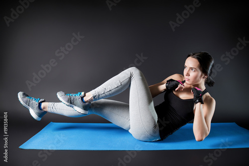 Sporty sexy girl doing exercises on the press while lying on the yoga mat. Black background.